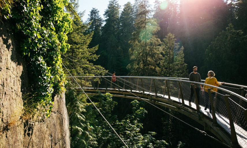 Guests enjoy a scenic walk along the Cliffwalk attraction on a sunny summer day at Capilano Suspension Bridge Park, immersed in breathtaking views and thrilling experiences