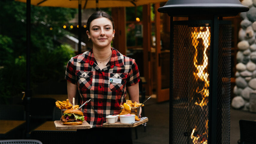 A team member walks out of the Cliff House Restaurant with plates of food in hand, ready to serve guests with delicious meals and warm hospitality at Capilano Suspension Bridge Park