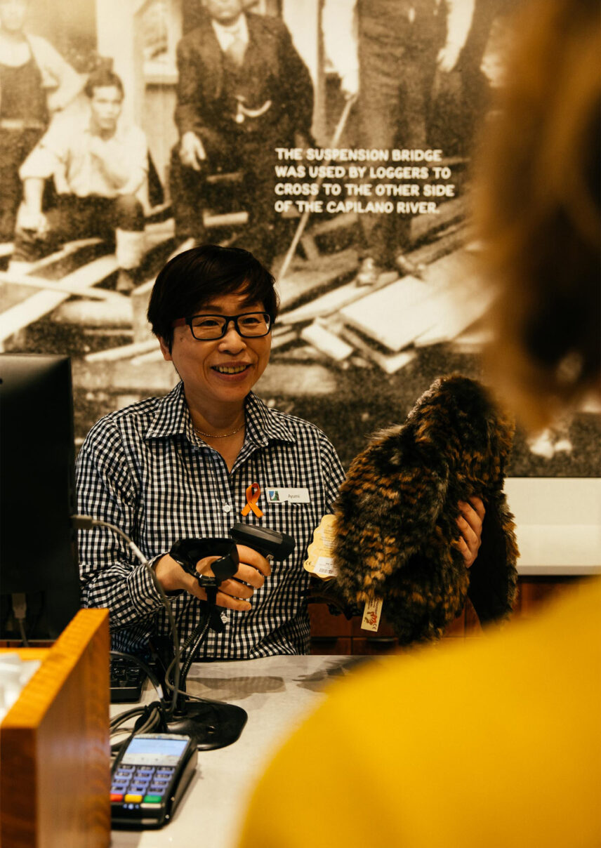 A team member smiles at a guest while scanning a stuffed animal toy they purchased in the Treading Post Gift Shop, providing friendly service and assistance at Capilano Suspension Bridge Park.