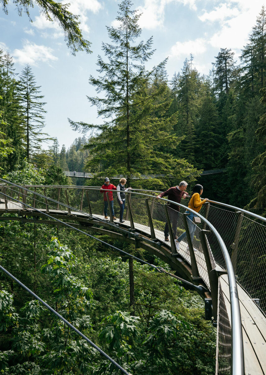 Guests enjoy a scenic walk along the Cliffwalk attraction at Capilano Suspension Bridge Park, immersed in breathtaking views and thrilling experiences with the Capilano Suspension Brige stretching across the canyon in the distance.