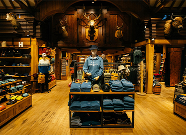 The grand entrance of the Trading Post Gift Shop features wooden fixtures, mounted animal heads, and an array of clothing items, inviting guests to explore a rustic and eclectic shopping experience at Capilano Suspension Bridge Park