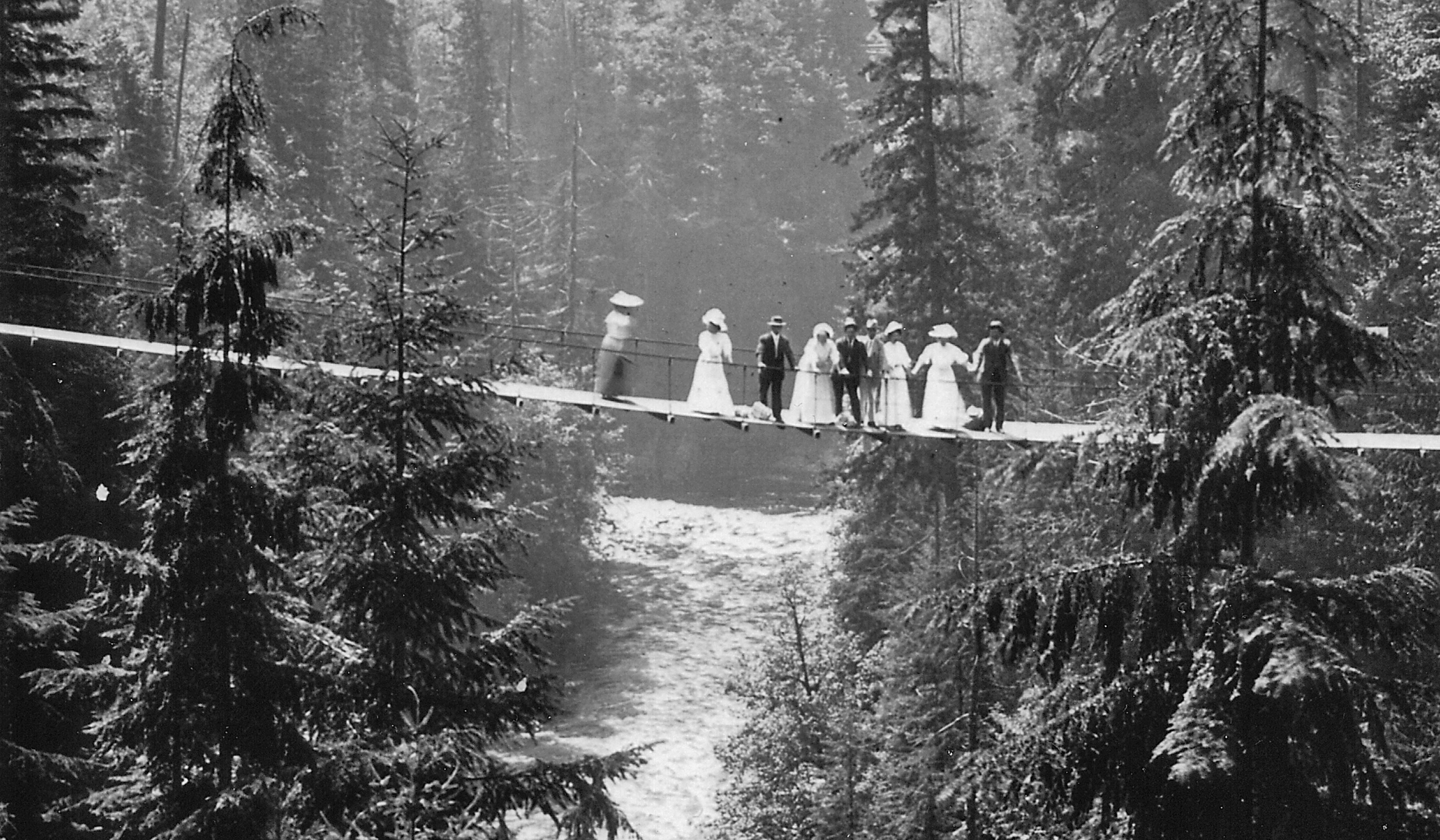 A historical black and white photo captures a wedding party on the first Capilano Suspension Bridge in 1889, offering a glimpse into the bridge's early days and its significance as a landmark for celebrations and gatherings